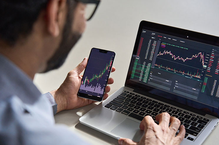 man on laptop and phone looking at stock market