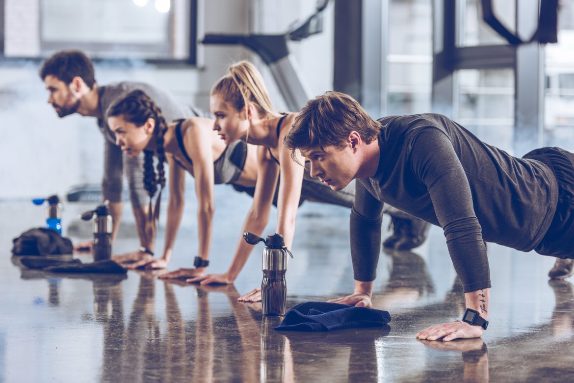 group of athletic young people in sportswear doing push ups or plank at the gym, group fitness