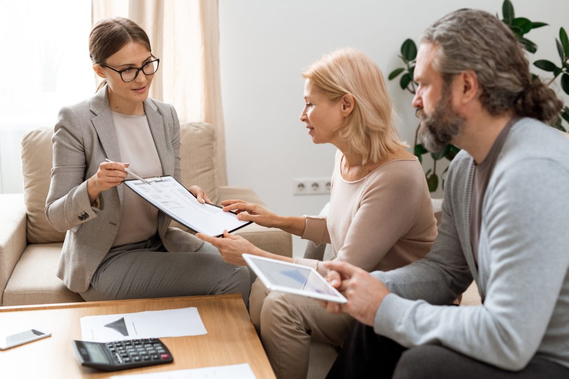 Young real estate agent pointing at document while consulting mature clients